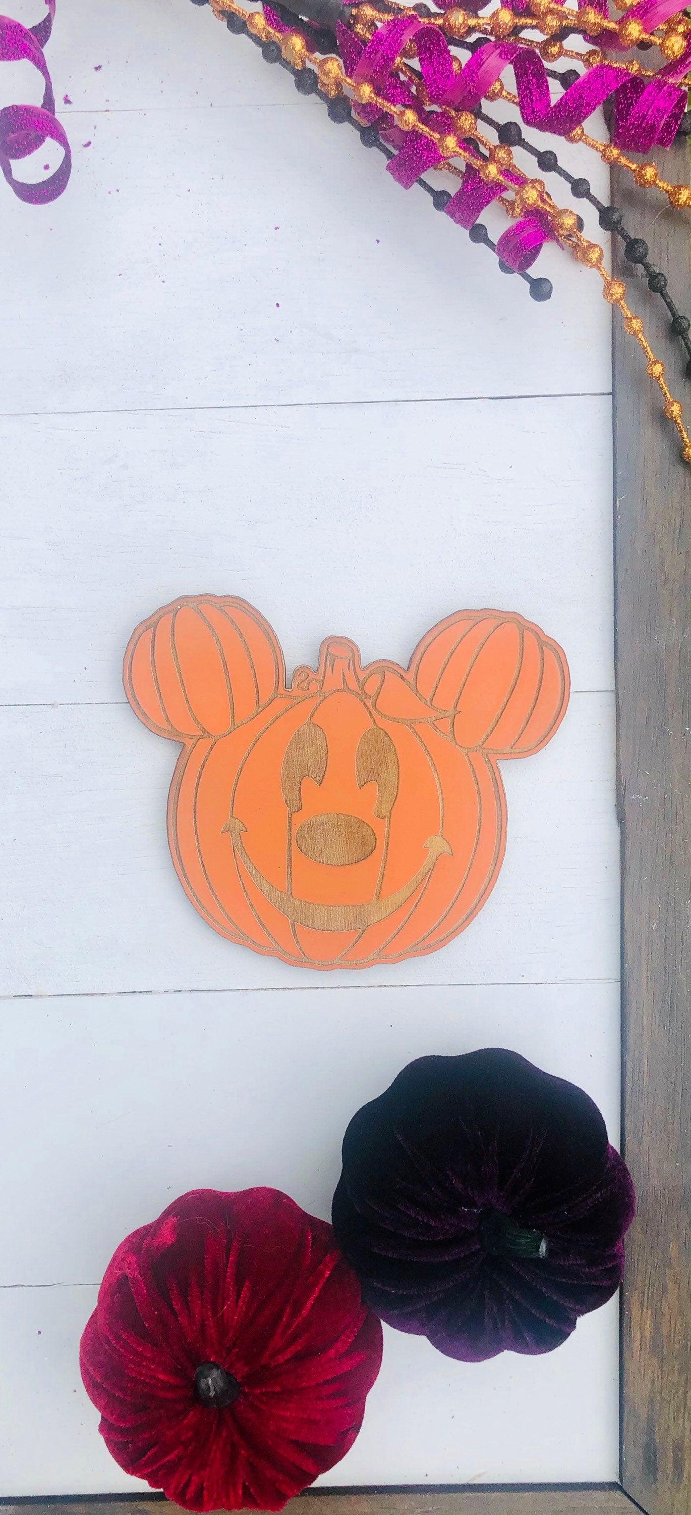 Decorative pumpkin with Mickey Mouse ears on a white surface with red and black flowers.