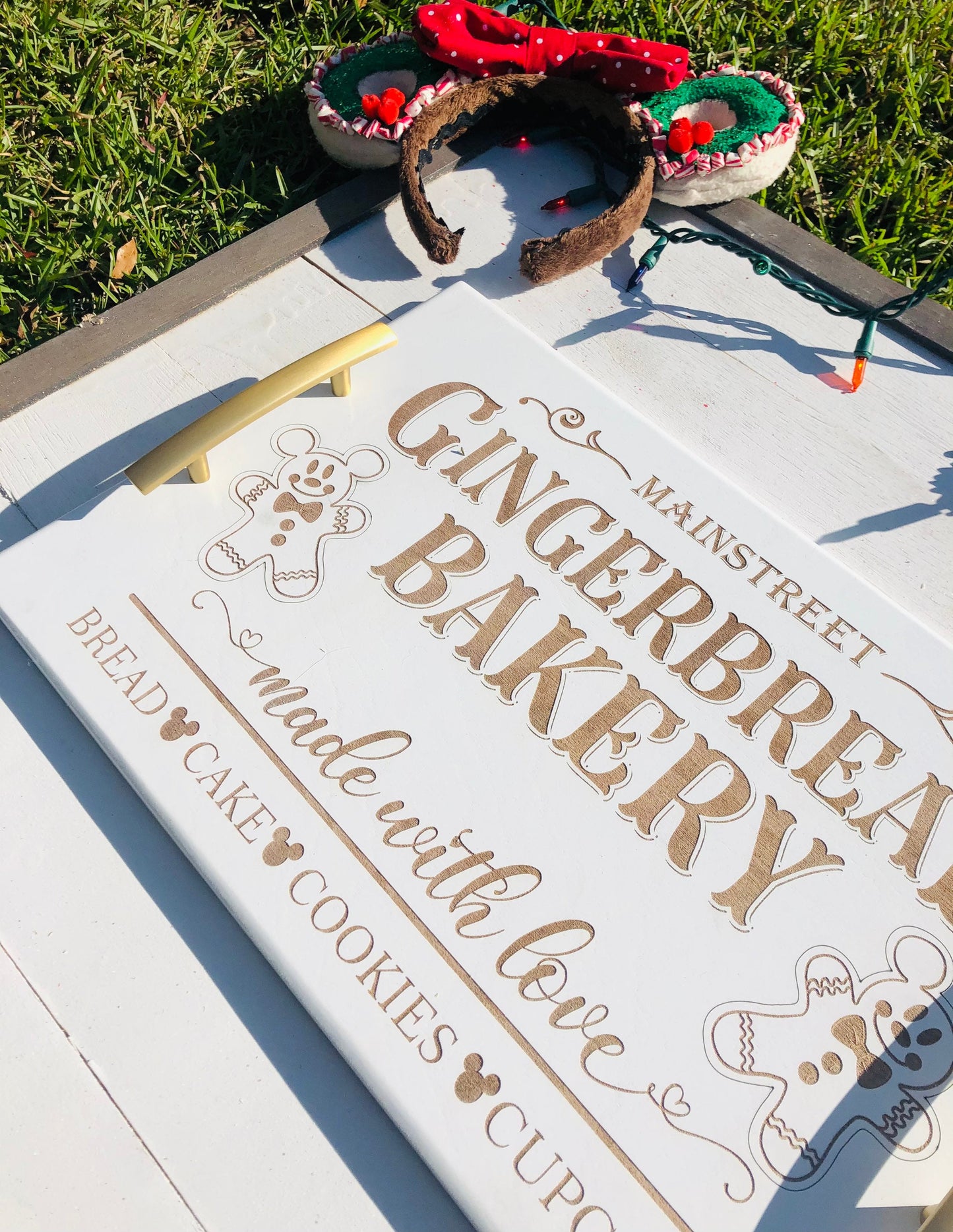 Gingerbread-themed bakery sign with a decorative headband on a grassy background