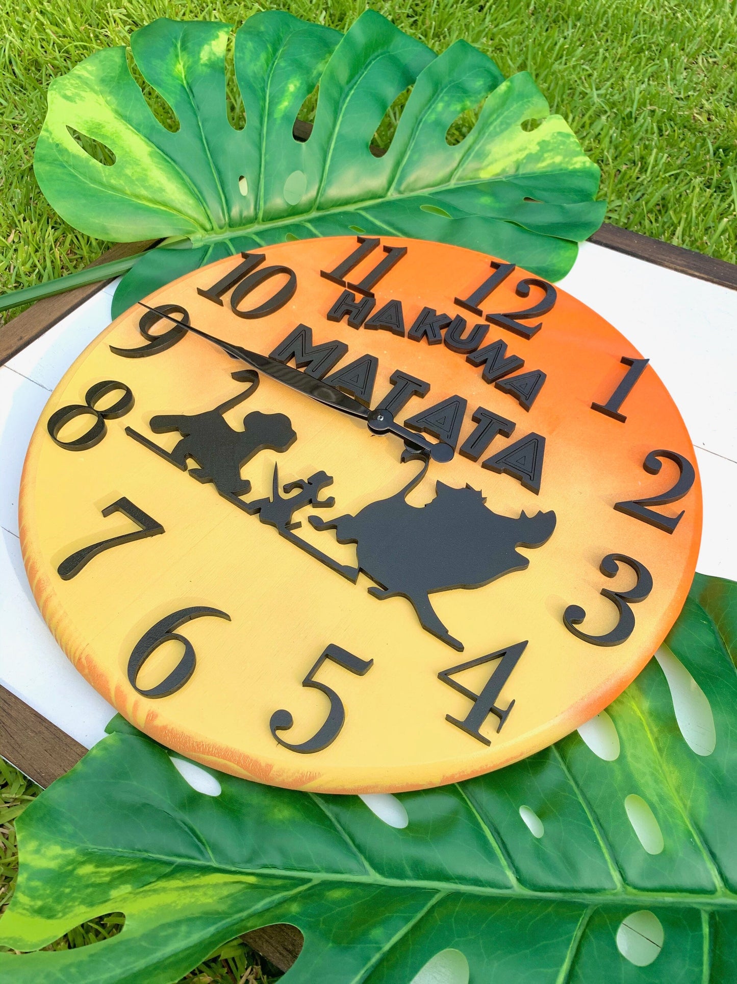 Pineapple-shaped clock with 'Hakuna Matata' text and cartoon characters on a grass background