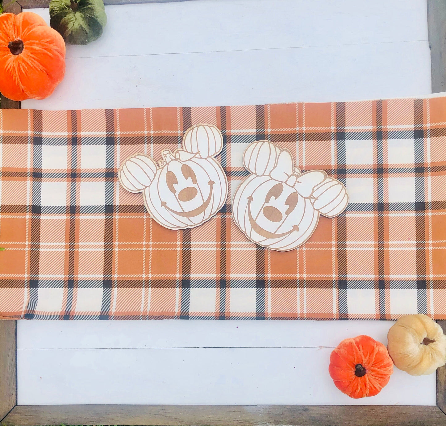 Plaid tablecloth with pumpkin-shaped cutouts on a wooden surface with small pumpkins.