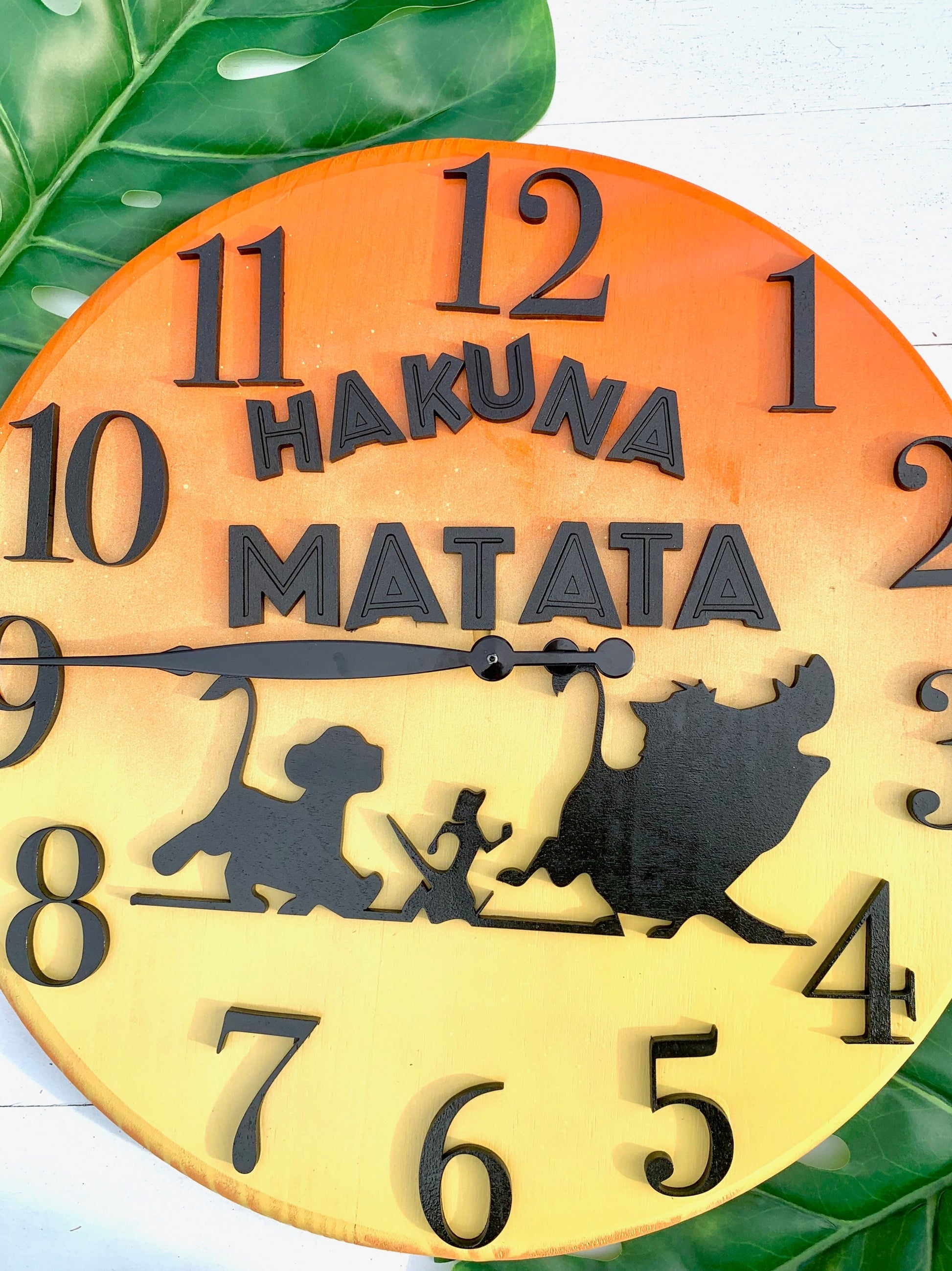 Decorative clock with 'Hakuna Matata' text and characters, surrounded by leaves.