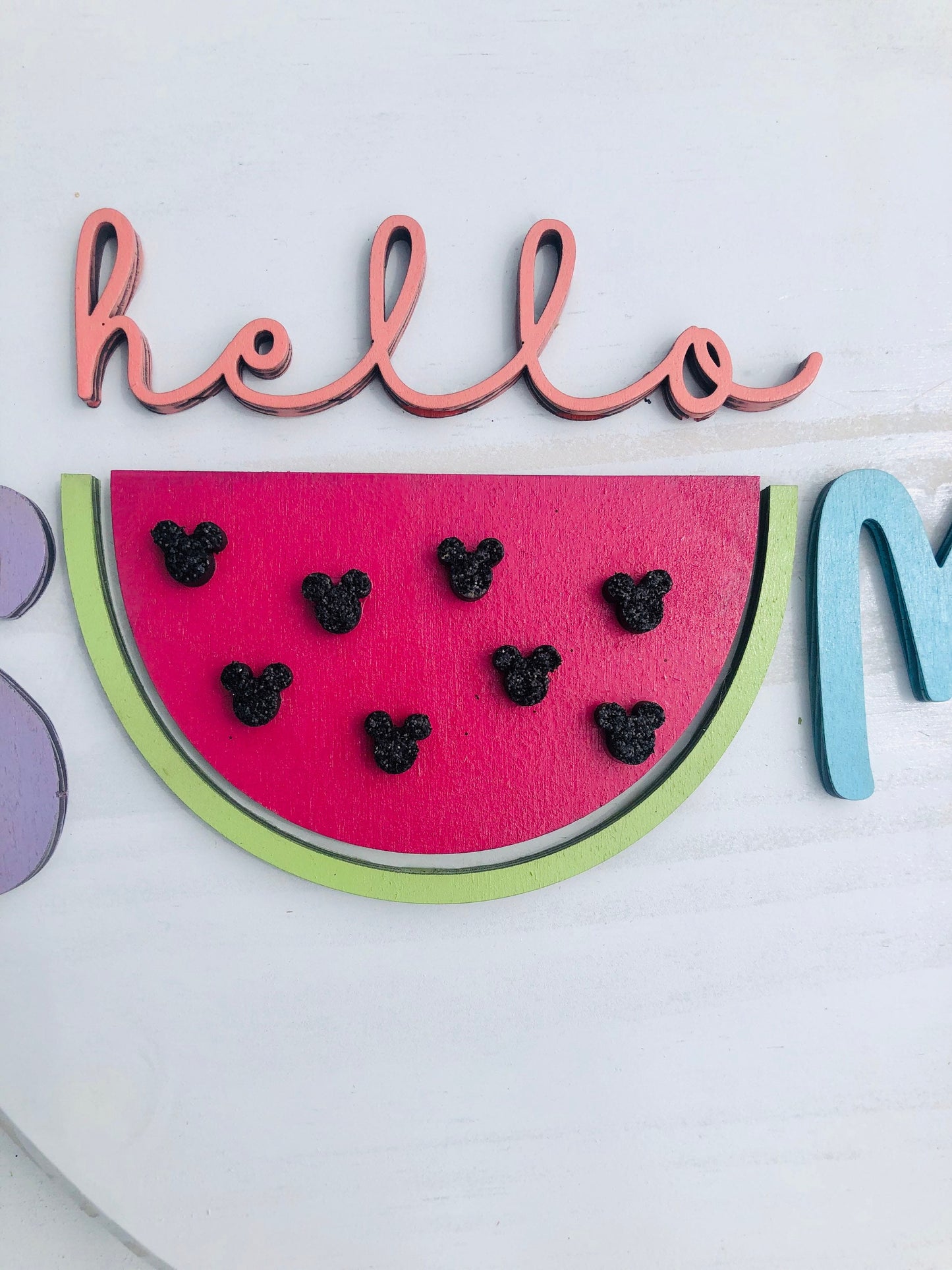 Decorative sign with watermelon slice, black dots, and 'hello' and 'mom' text on a white background