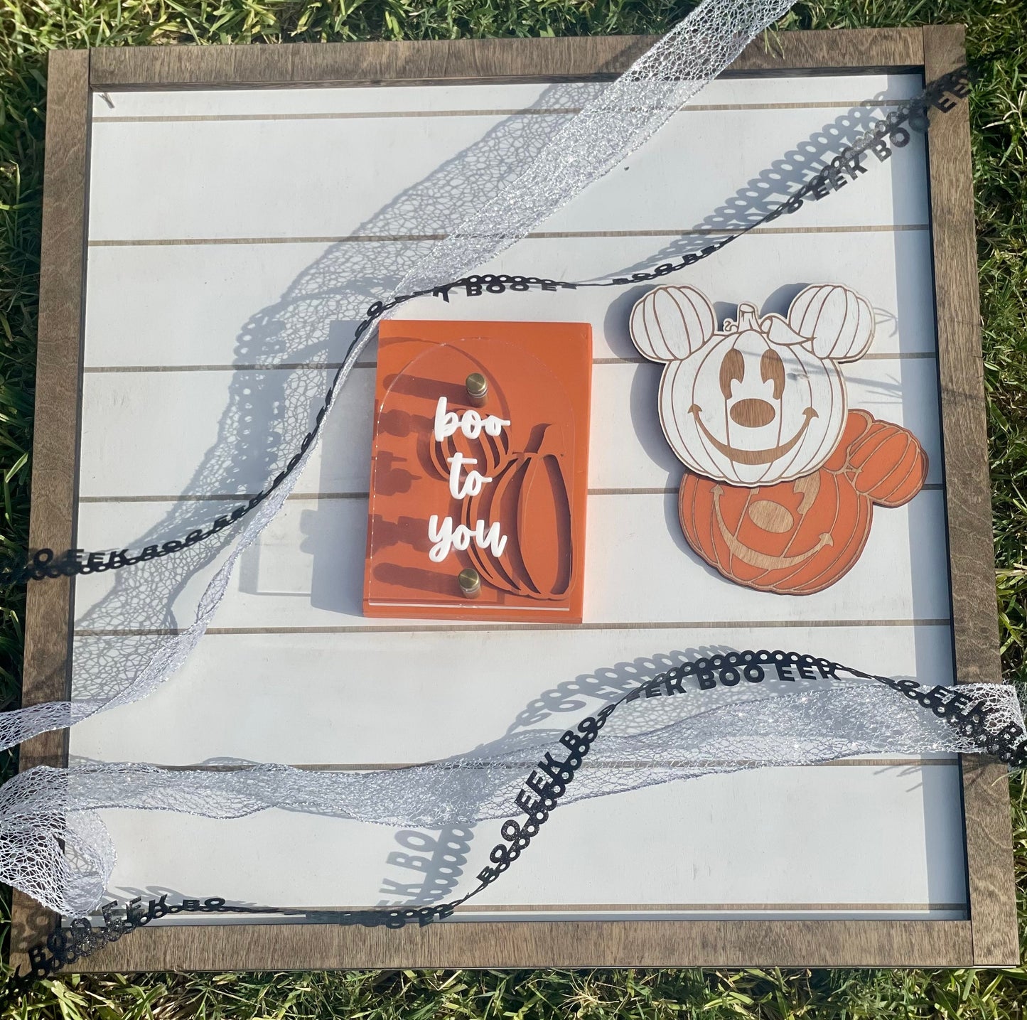 Decorative sign with Halloween-themed design featuring a pumpkin and text on a grass background.