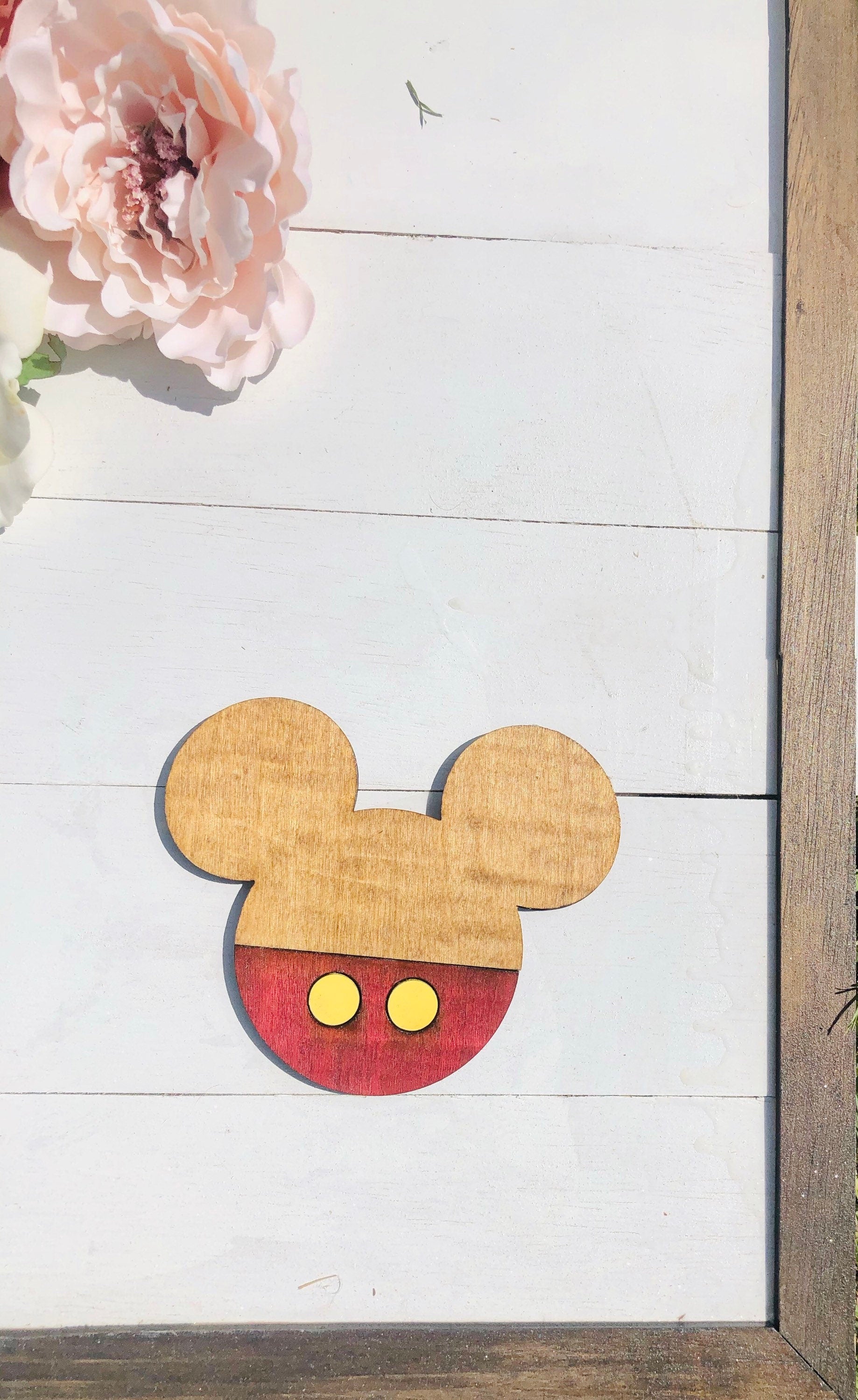Wooden cutout of a mouse head design on a white wooden surface with pink flowers.