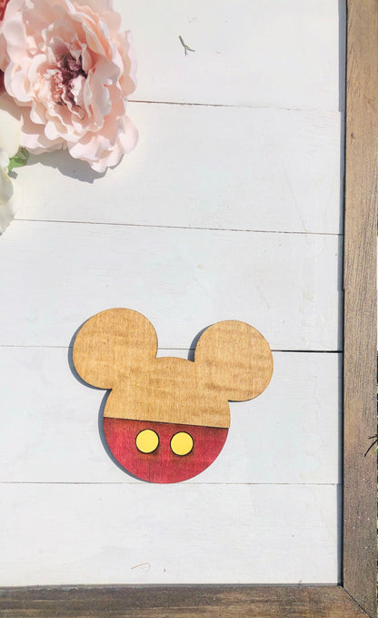 Wooden cutout of a mouse head design on a white wooden surface with pink flowers.