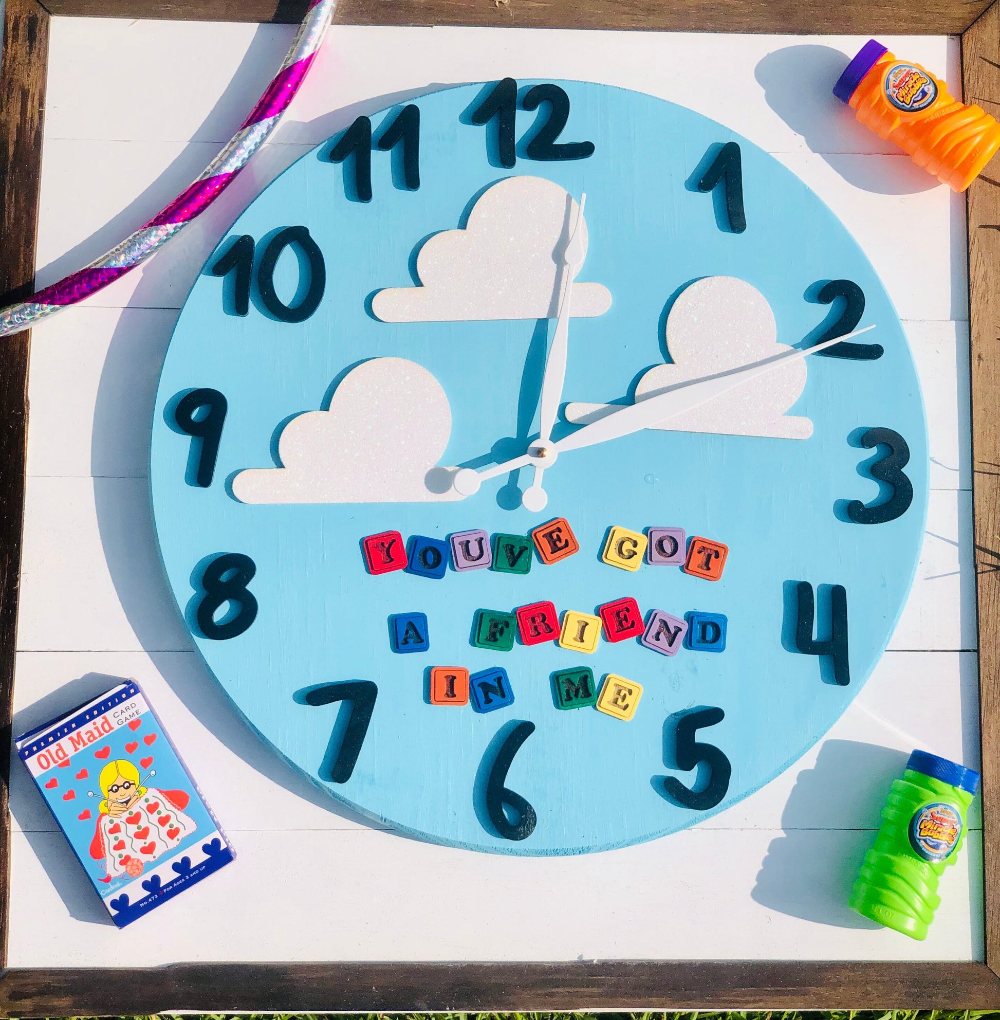 Children's clock with colorful letters spelling out a message, surrounded by toys on a wooden surface.