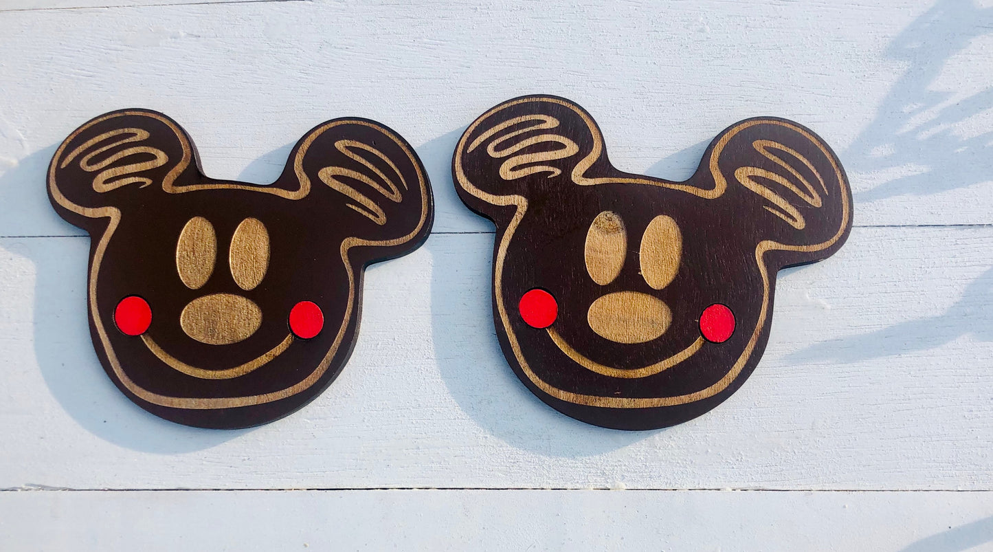 Two wooden Mickey Mouse head cutouts on a light blue wooden surface.
