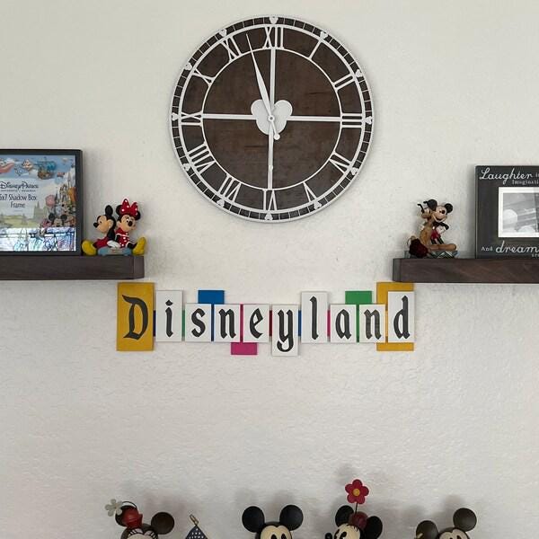 Decorative wall with a large clock, Disney-themed figurines, and 'Disneyland' sign.