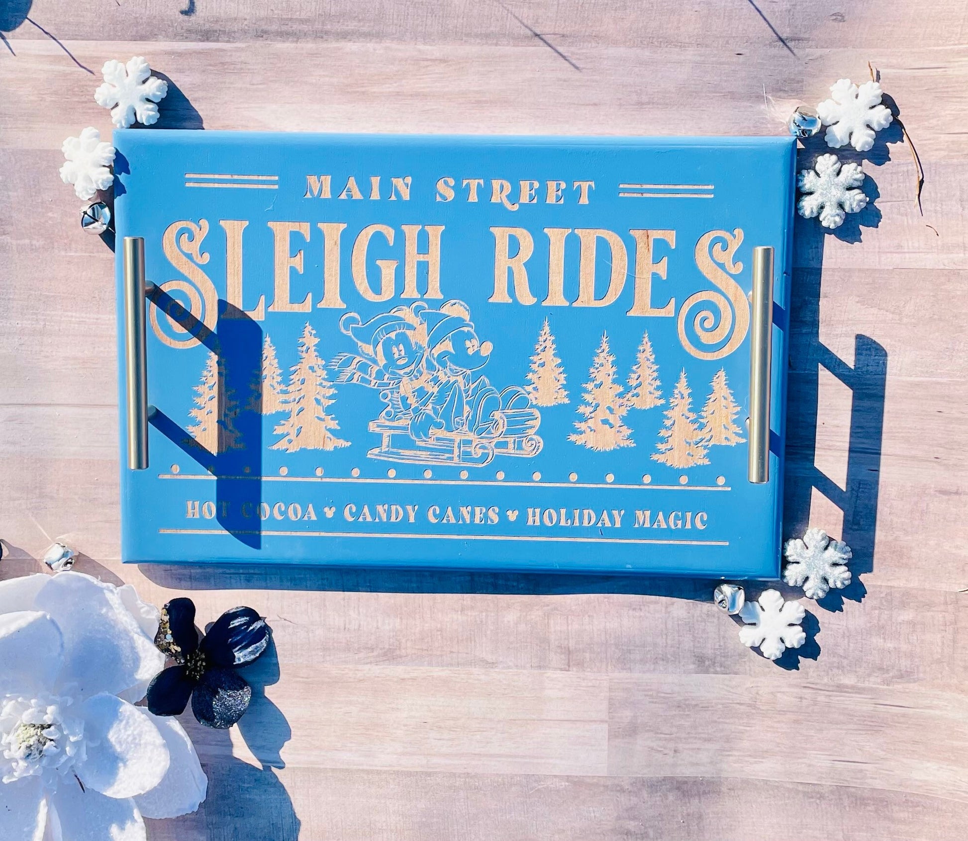 Blue tray with 'Main Street Sleigh Rides' design on a wooden surface with white flowers.