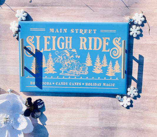 Blue tray with 'Main Street Sleigh Rides' design on a wooden surface with white flowers.
