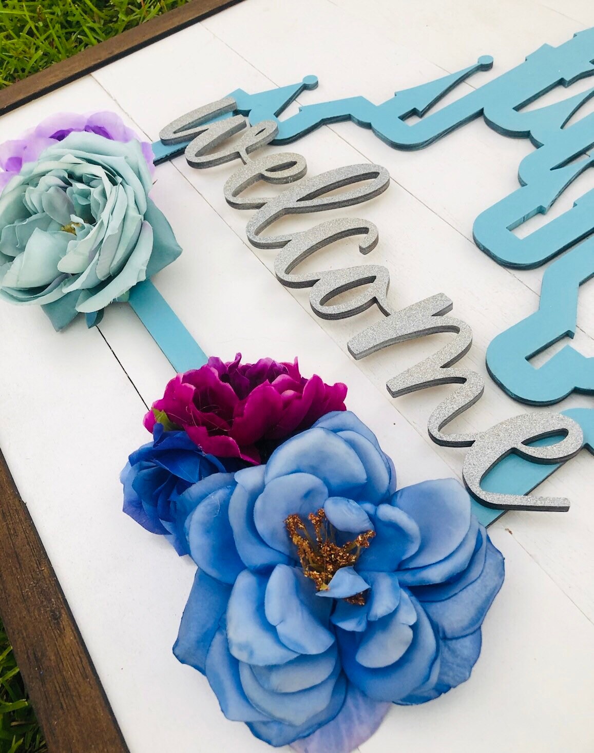 Decorative sign with flowers and 'Welcome' text on a white surface.