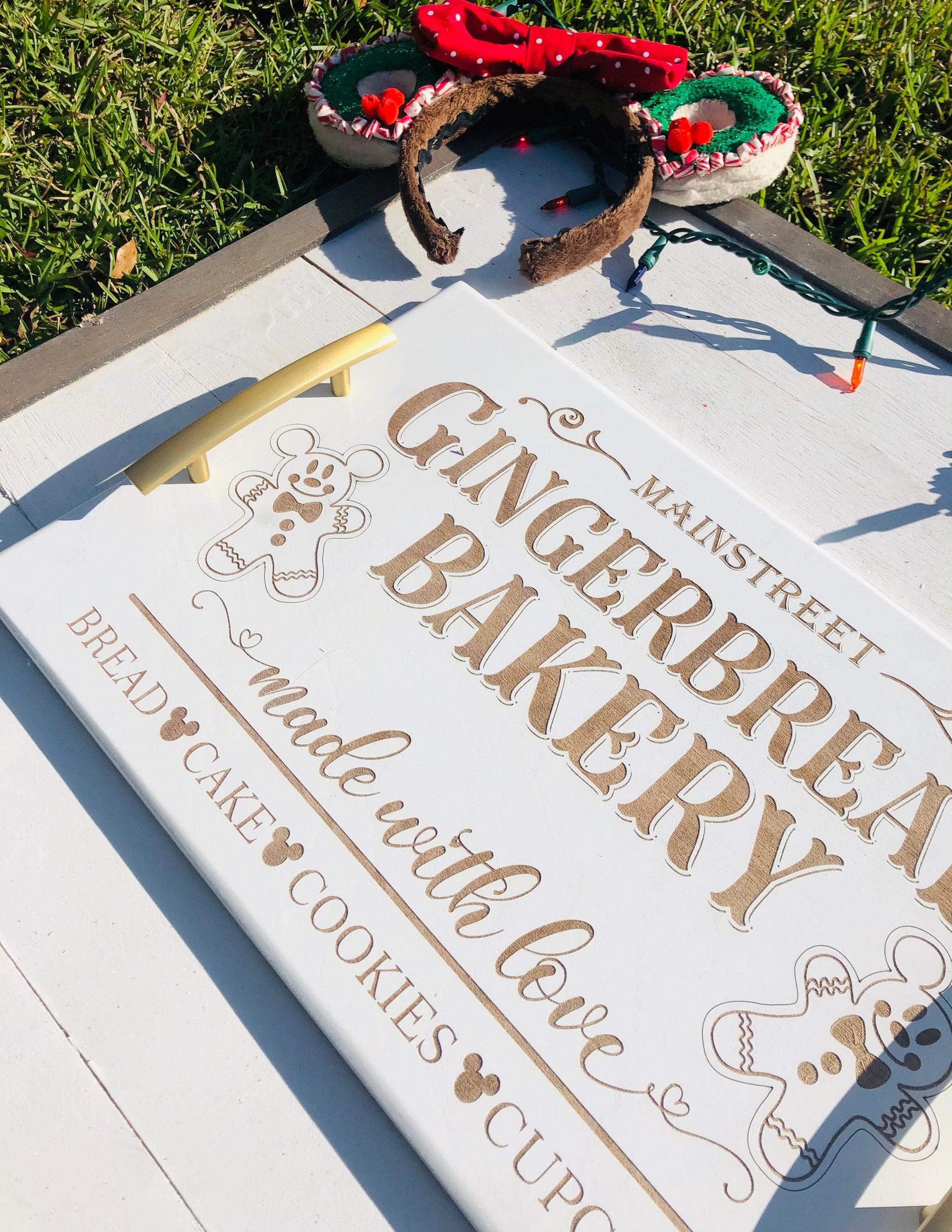 Gingerbread-themed bakery sign with a decorative headband on a grassy background