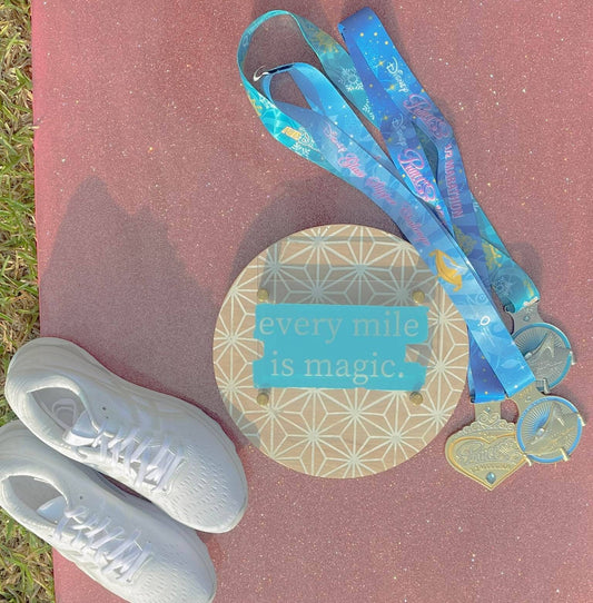 White running shoes, colorful lanyard, and circular sign with 'every mile is magic' text on a red surface.
