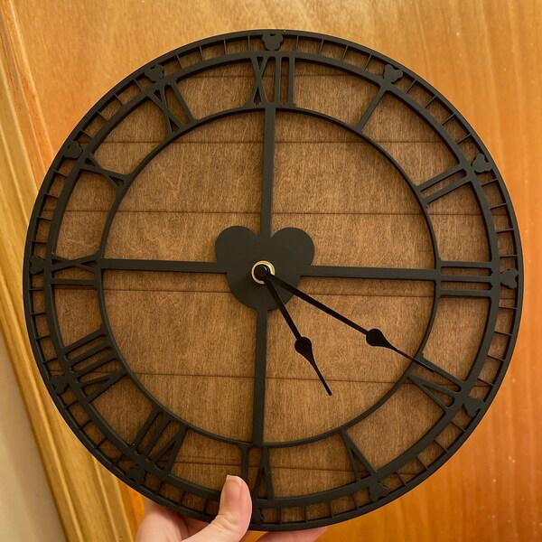 Large round clock with black Roman numeral details held against a wooden background