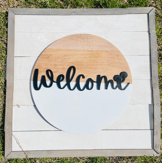Wooden sign with 'Welcome' text on a circular design, outdoors.