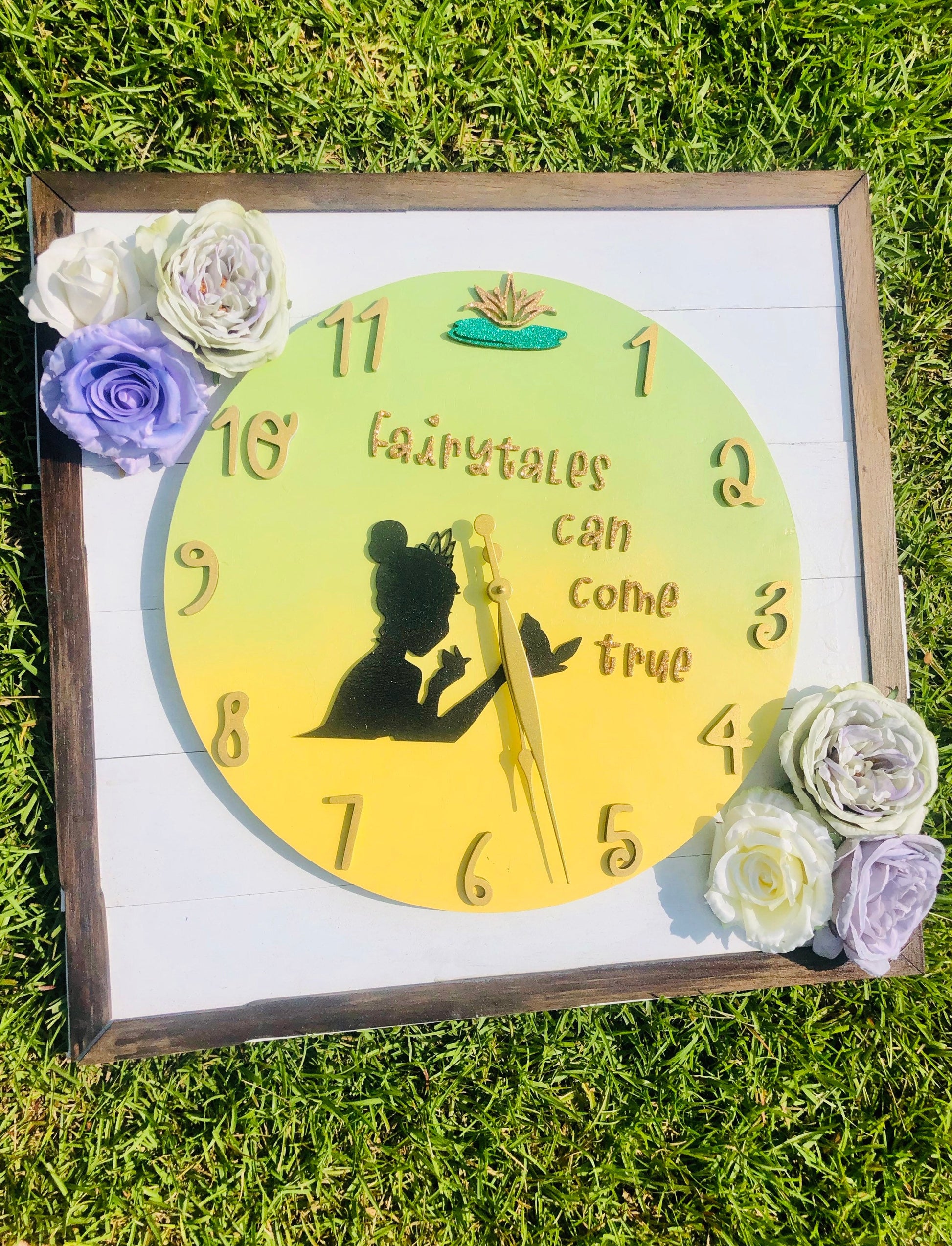 Decorative clock with fairy silhouette and 'Fairytales can come true' text, surrounded by flowers on grass.