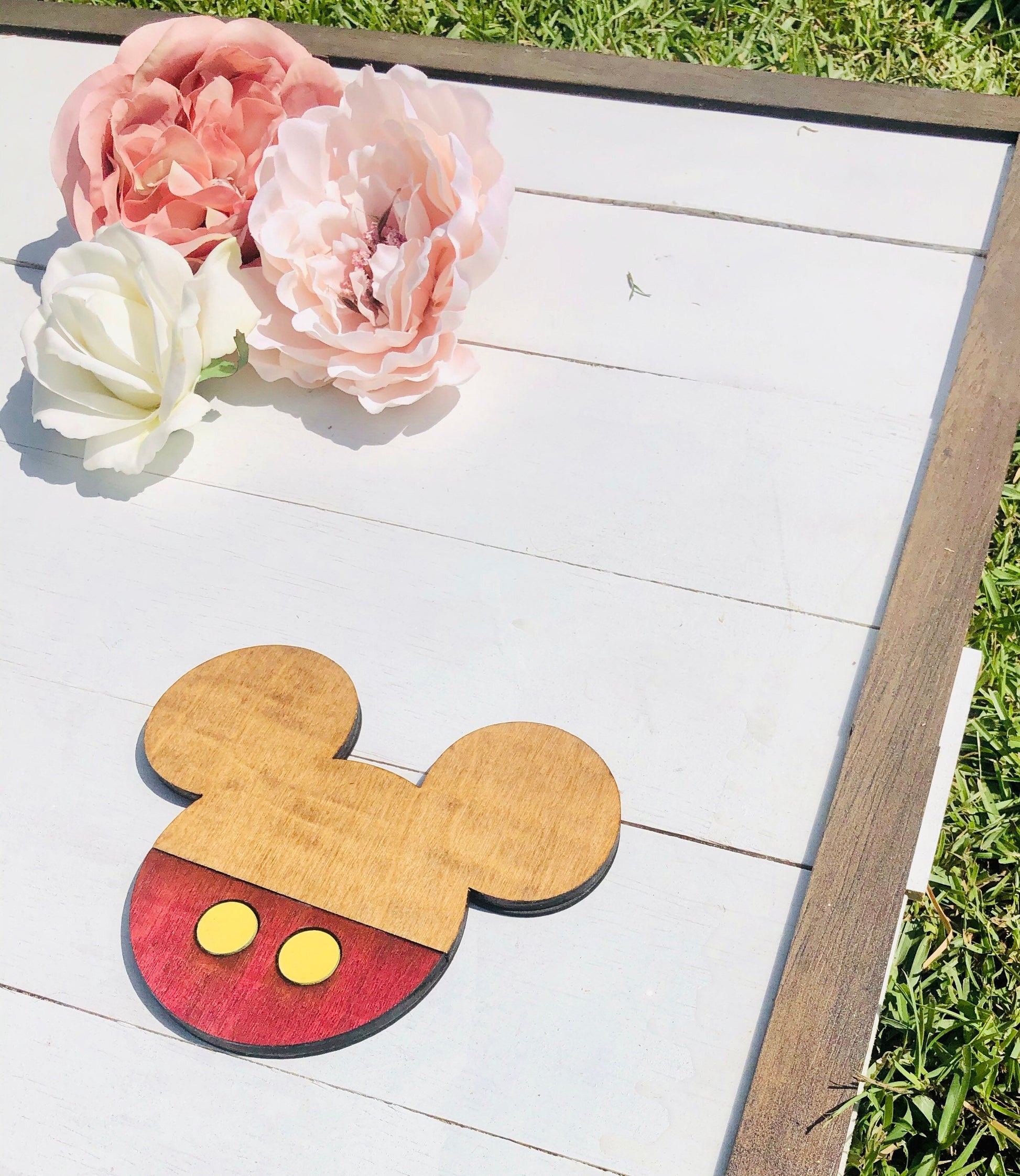 Wooden cutout of a mouse head with pink and white flowers on a wooden surface.