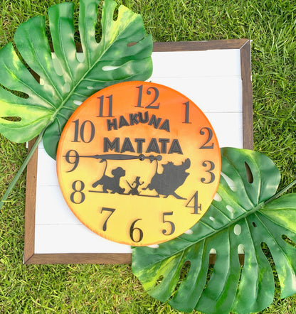 Round clock with 'Hakuna Matata' text and characters on a white background with green leaves.