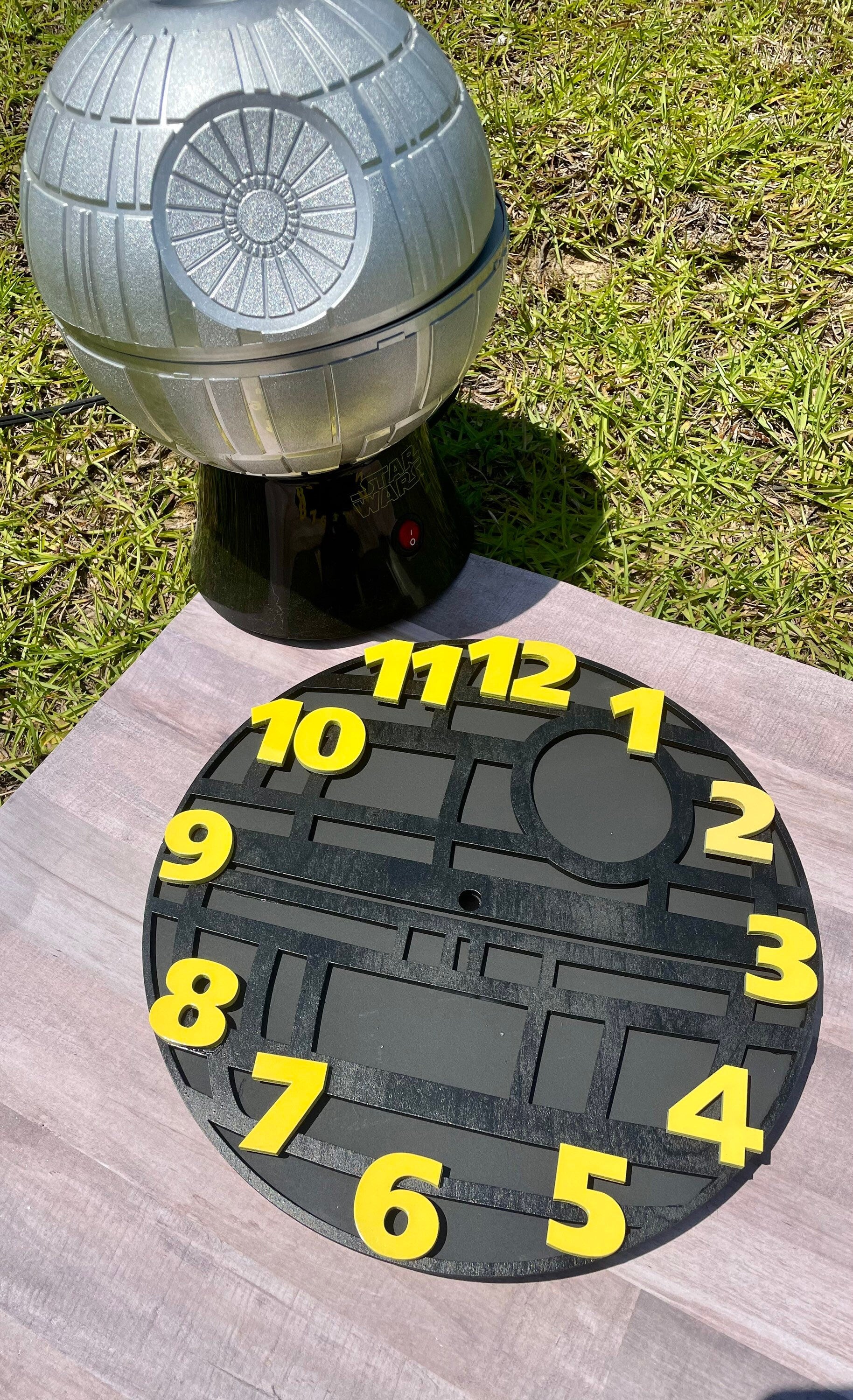 Death Star-themed clock on a wooden surface with grass in the background