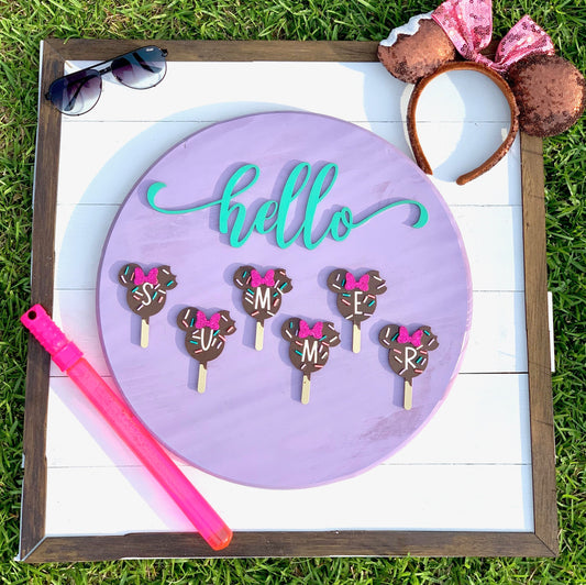 Decorative sign with 'hello' in teal, chocolate cake pops with pink bows, and a pink straw on a grass background.