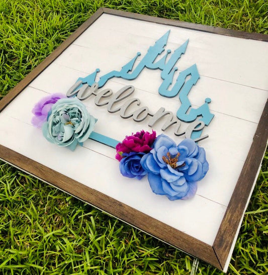 Decorative sign with 'Welcome' and floral elements on a grass background