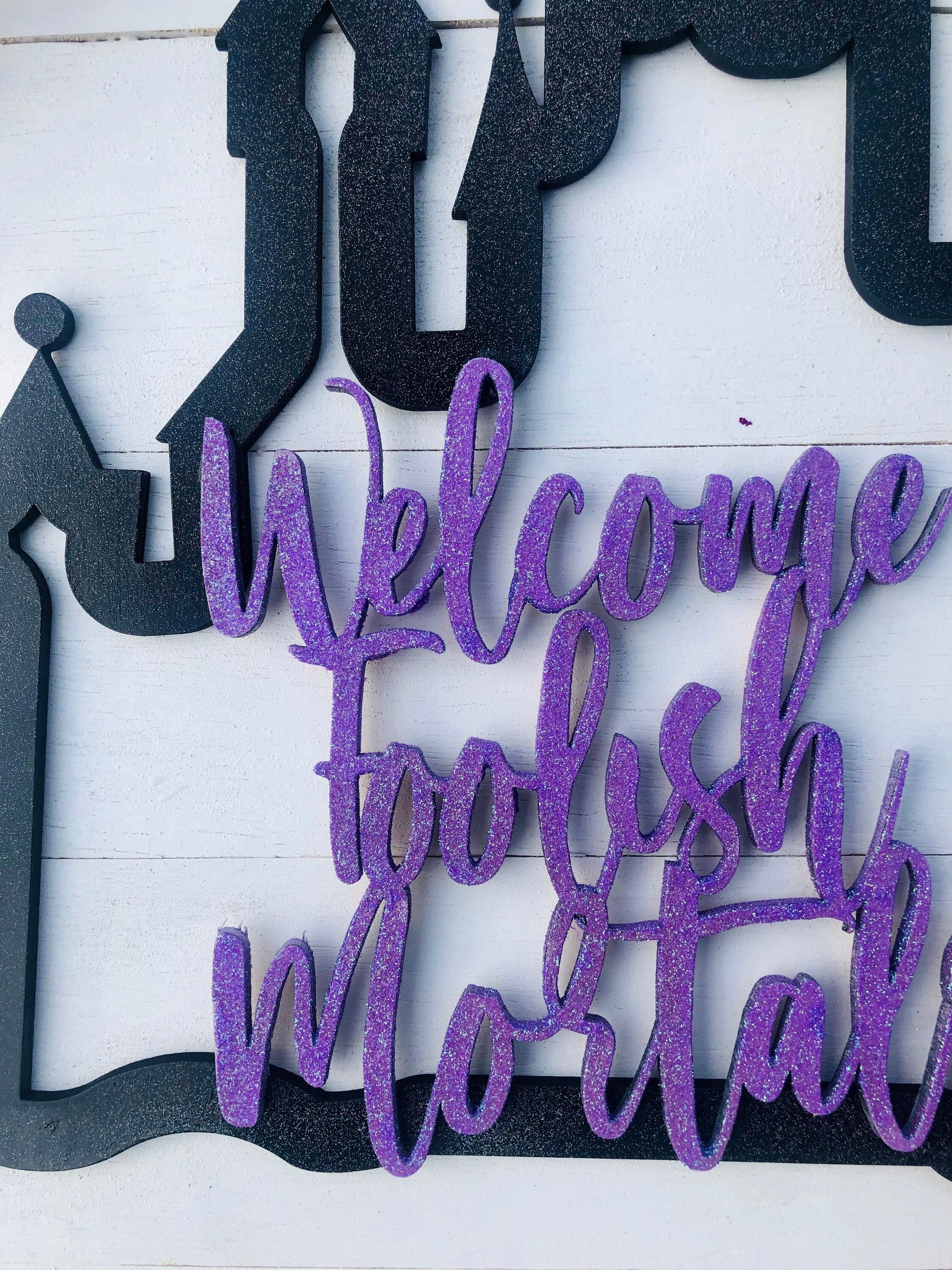 Decorative sign with purple text 'Welcome to the Mortal' on a white background