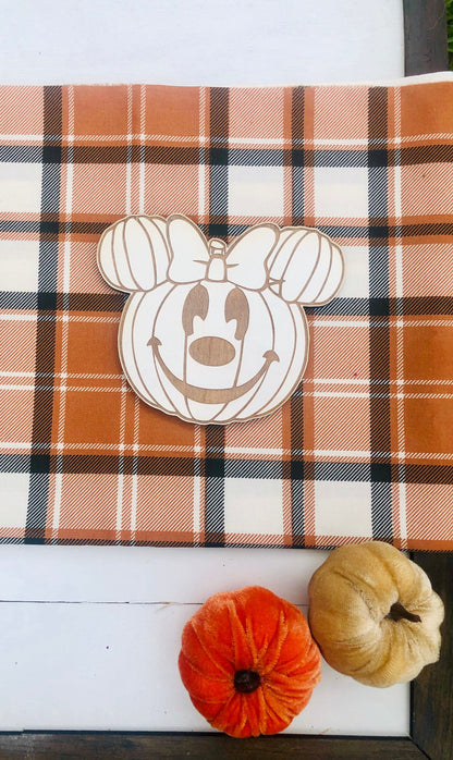 Pumpkin-shaped cutout with Minnie Mouse design on a plaid fabric background with small pumpkins.