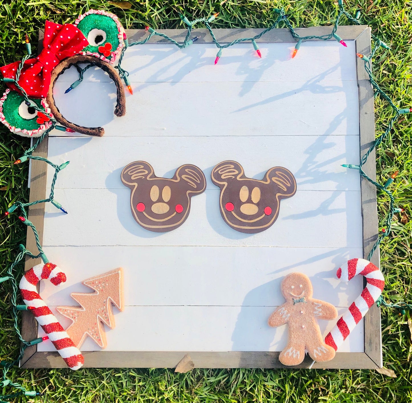 Decorative gingerbread cookies shaped like Mickey Mouse, a tree, and a person on a wooden board with Christmas lights.