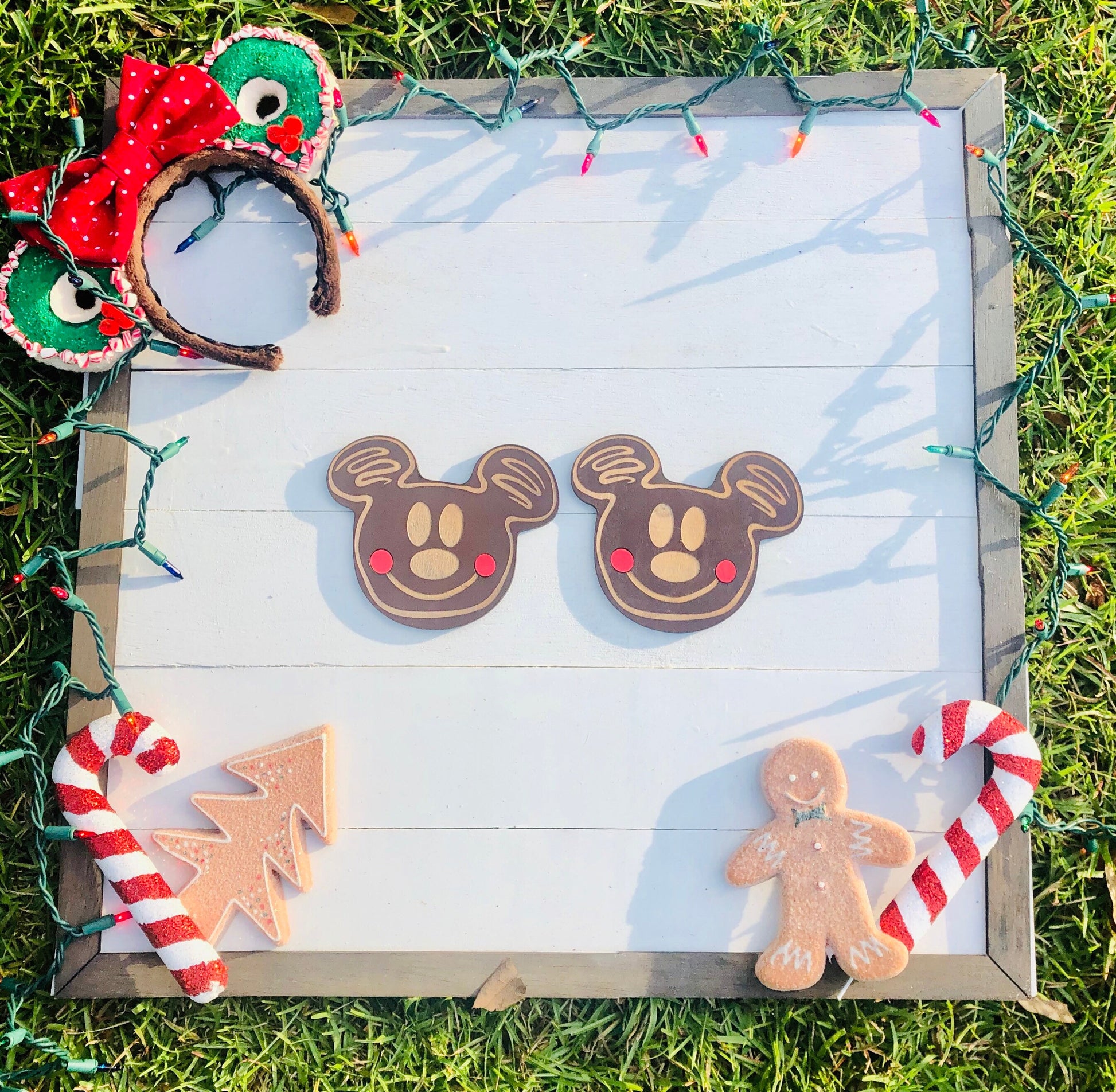 Decorative gingerbread cookies shaped like Mickey Mouse, a tree, and a person on a wooden board with Christmas lights.