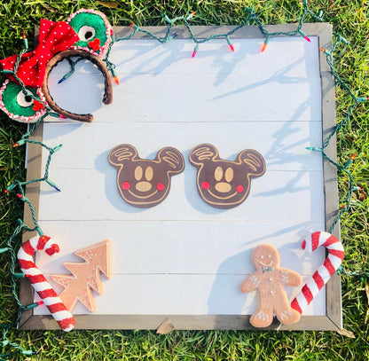Decorative gingerbread cookies shaped like Mickey Mouse, a tree, and a person on a wooden board with Christmas lights.
