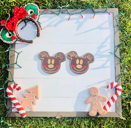 Decorative gingerbread cookies shaped like Mickey Mouse, a tree, and a person on a wooden board with Christmas lights.