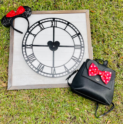 Black backpack with red polka dot bow next to a clock and Minnie Mouse ears on grass