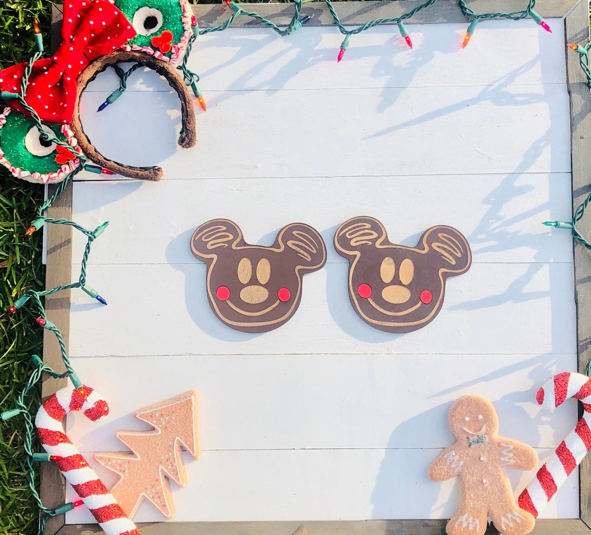 Two gingerbread cookies shaped like Mickey Mouse on a white wooden surface with Christmas decorations.