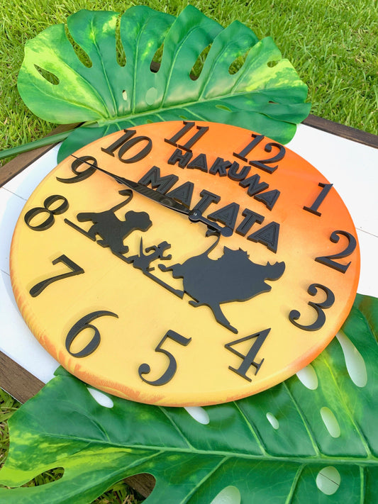 Pineapple-shaped clock with 'Hakuna Matata' text and cartoon characters on a grass background