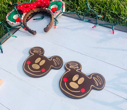 Two chocolate-shaped Mickey Mouse cookies on a wooden surface with Christmas lights in the background.