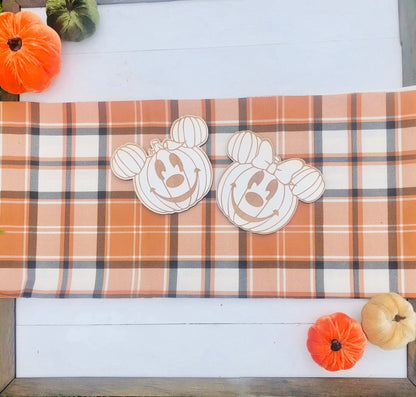 Plaid tablecloth with pumpkin-shaped cutouts on a wooden surface with small pumpkins.