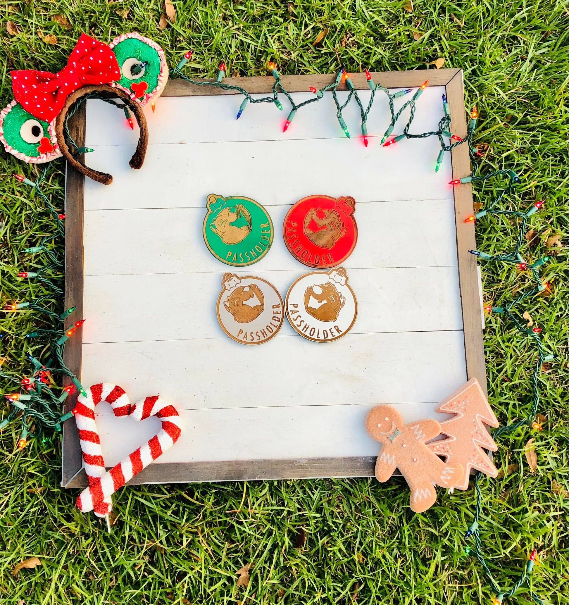 Set of Christmas-themed pins on a wooden board with decorative lights and ornaments on grass.