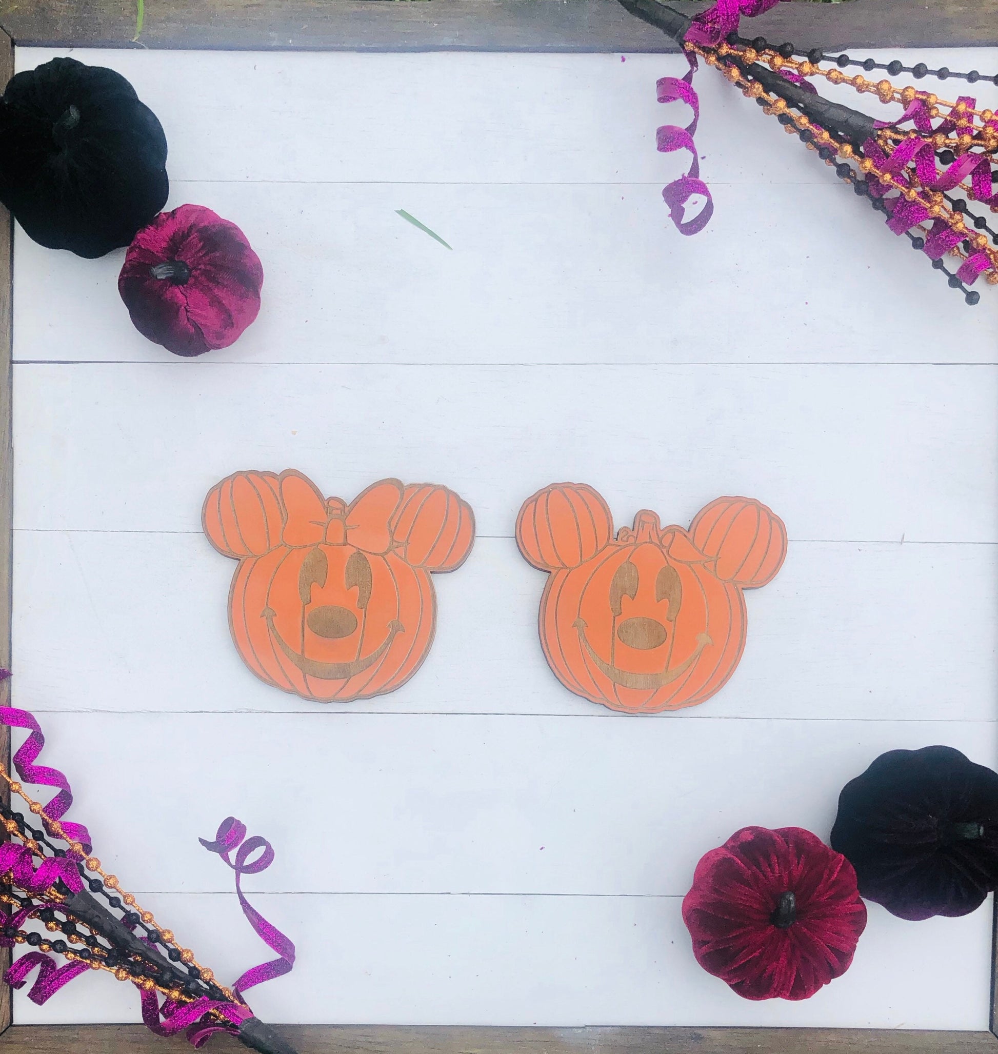 Two orange pumpkin designs with Mickey Mouse ears on a white wooden surface, surrounded by Halloween decorations.