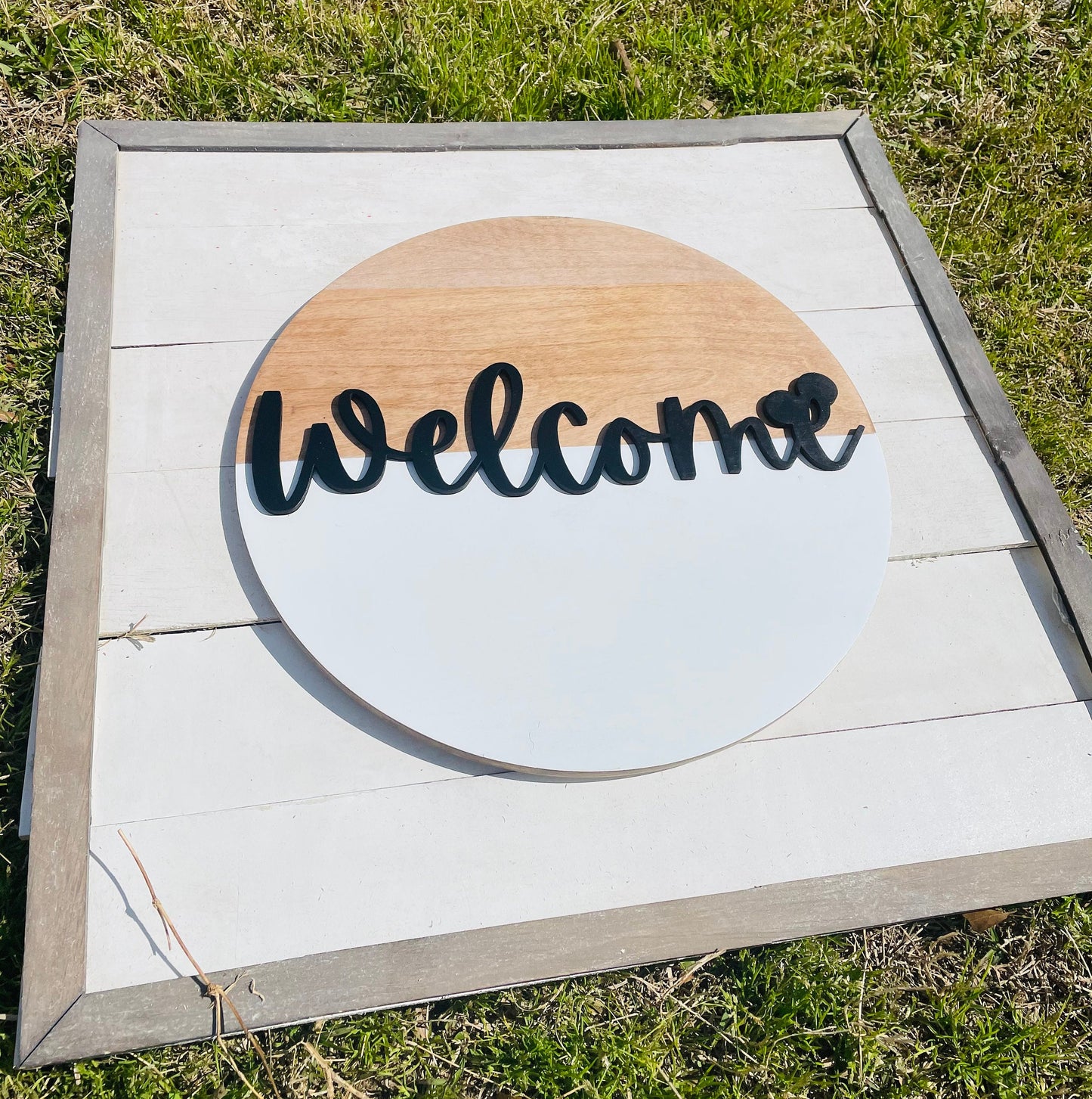Wooden sign with 'Welcome' text on a white background, outdoors.