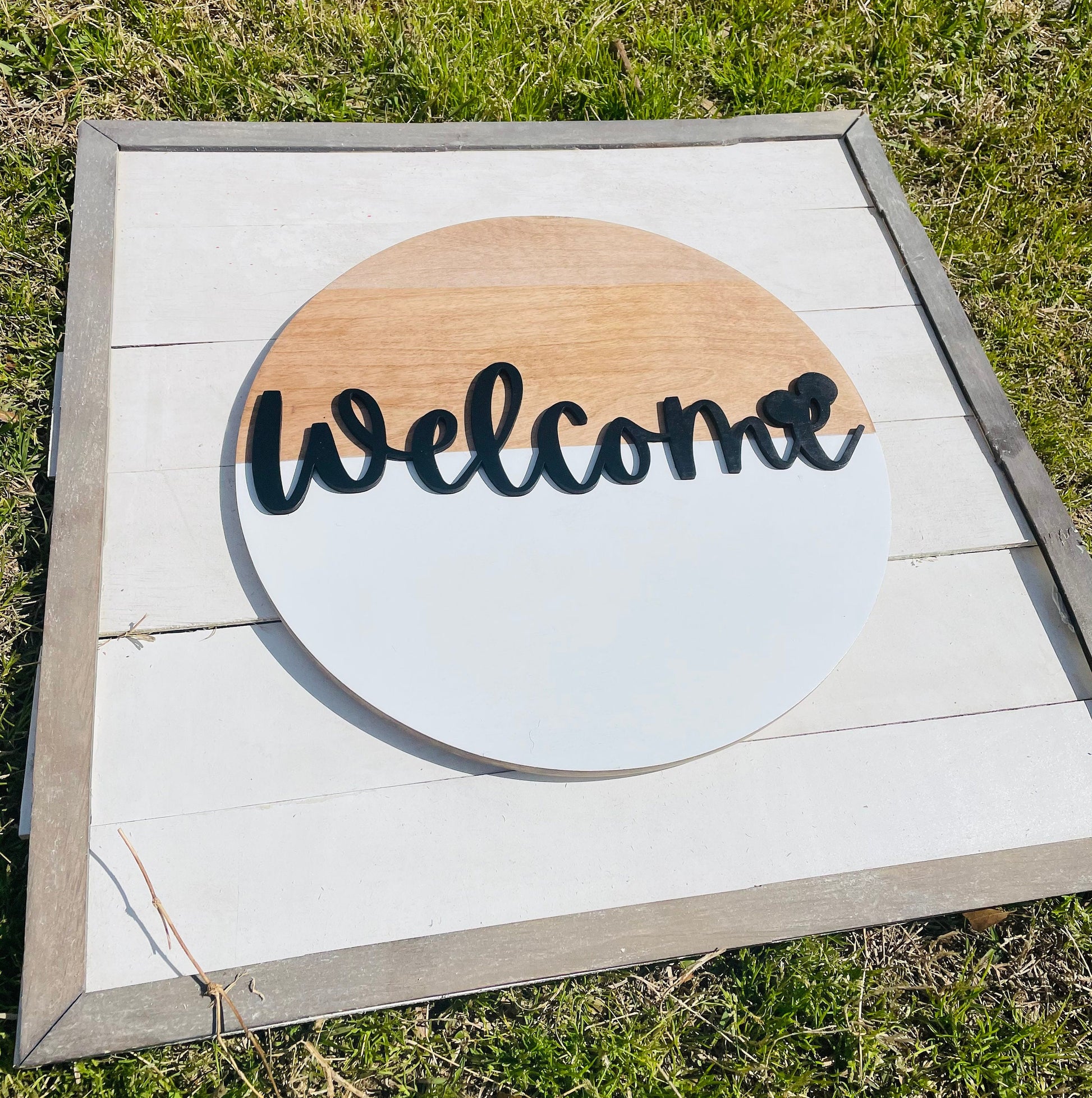Wooden sign with 'Welcome' text on a white background, outdoors.