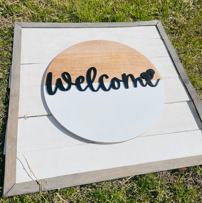 Wooden sign with 'Welcome' text on a white background, outdoors.