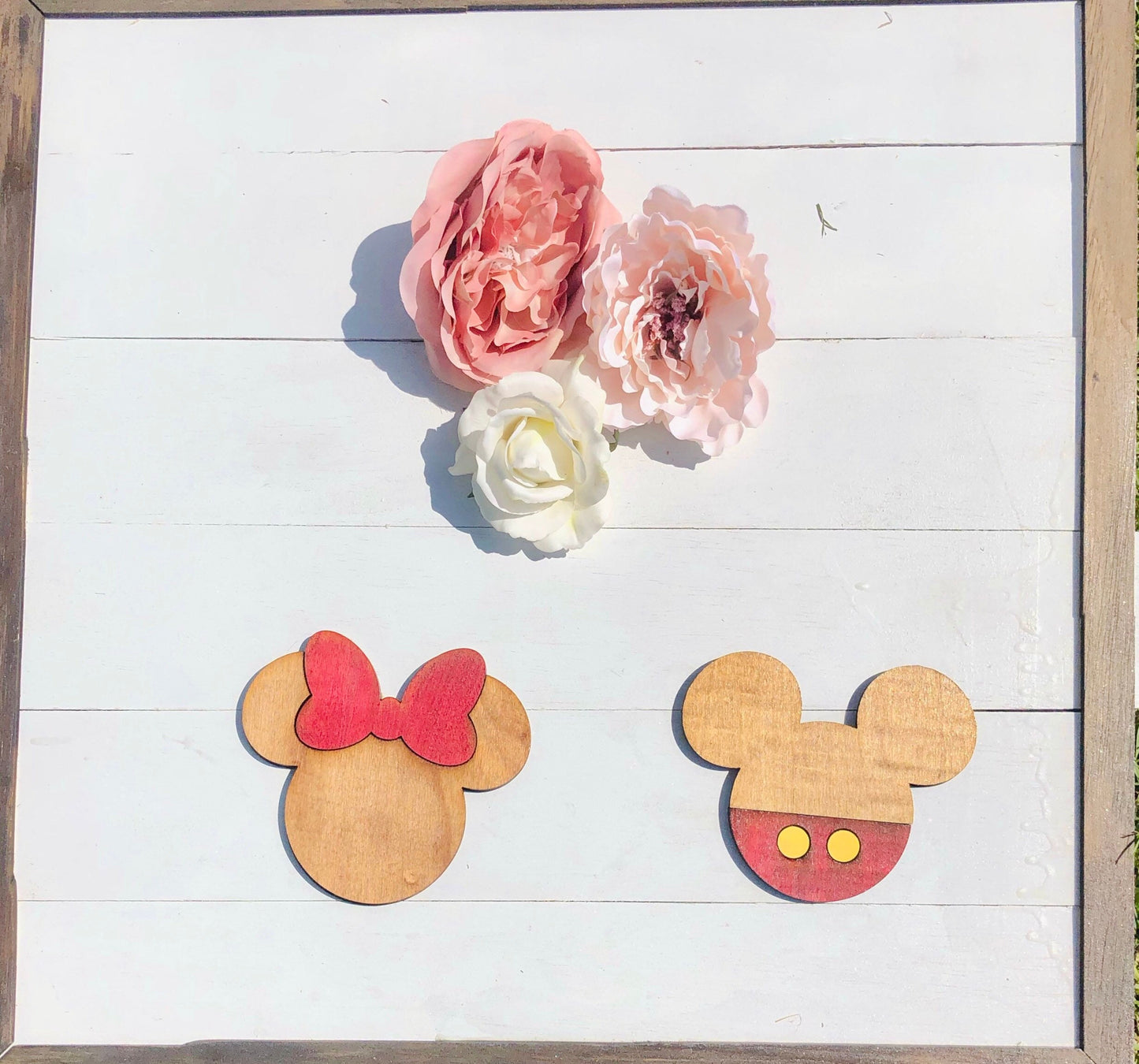 Wooden cutouts of Minnie and Mickey Mouse heads with flowers on a white wooden background