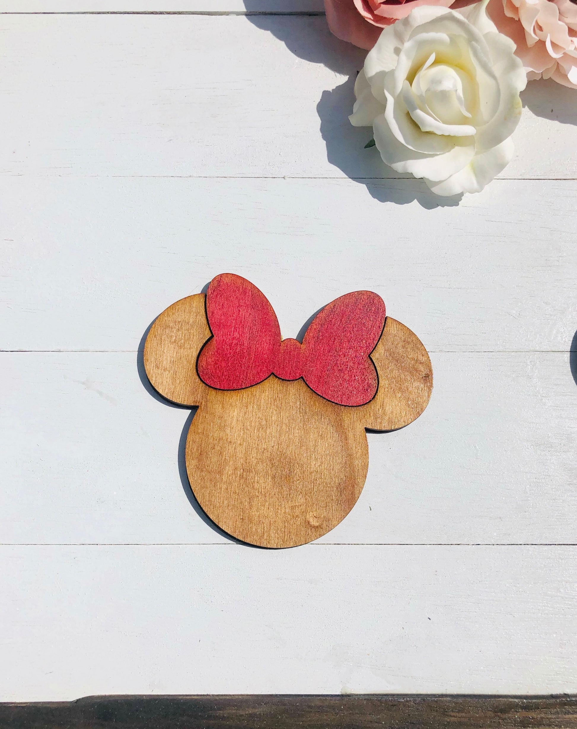 Wooden cutout of a character's head with a red bow on a white wooden surface with flowers.