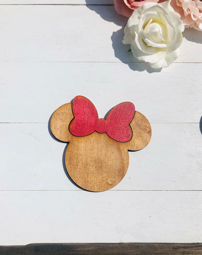 Wooden cutout of a character's head with a red bow on a white wooden surface with flowers.