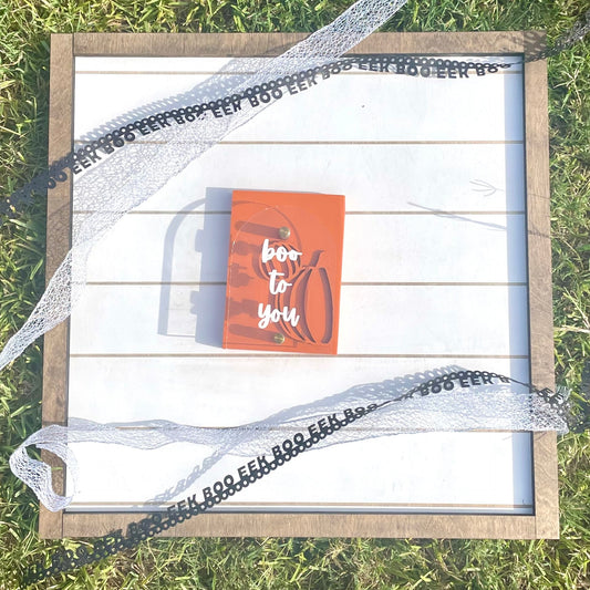 Wooden frame with a card inside, surrounded by decorative ribbons on grass