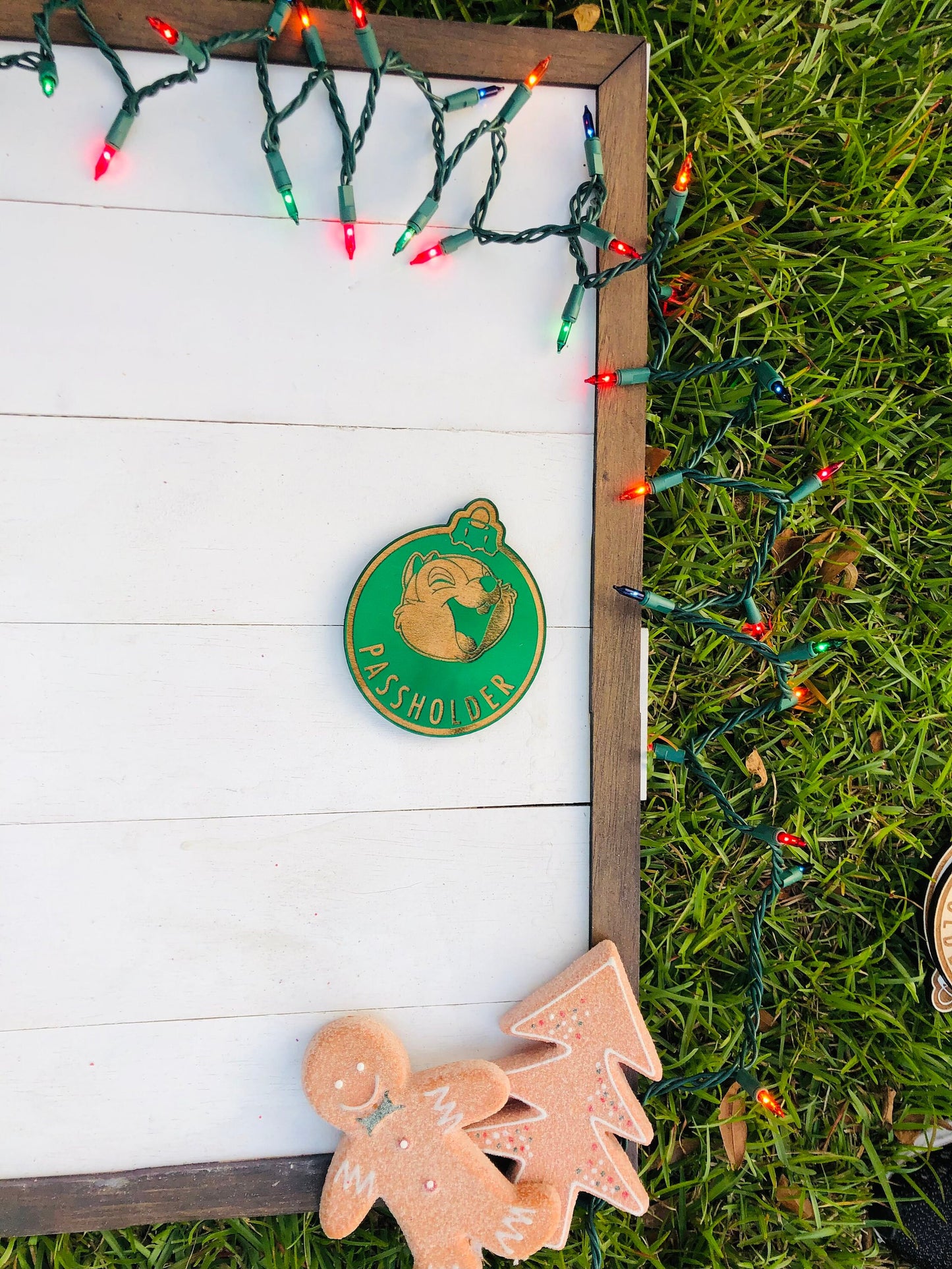 Decorative sign with a green logo and gingerbread cookies on grass with Christmas lights.