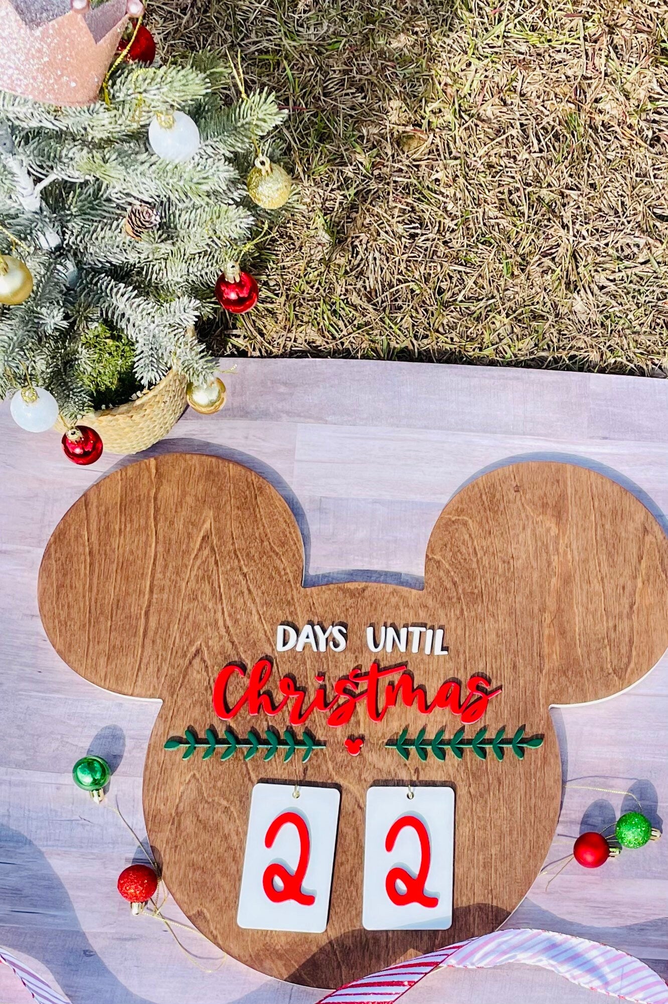 Wooden Christmas countdown calendar with Mickey Mouse design next to a decorated Christmas tree.
