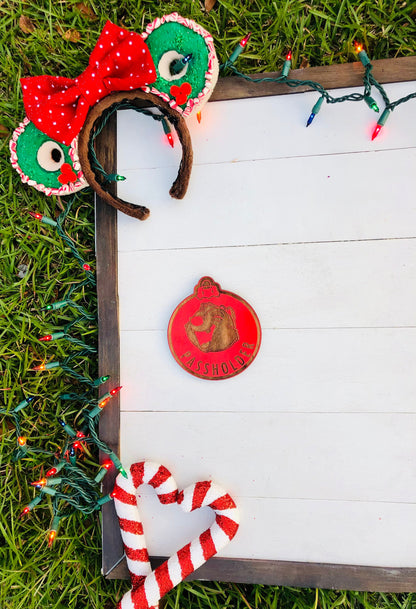 Decorative headbands with red bows and green accents, a candy cane, and a wooden ornament on a white surface with grass and lights in the background.