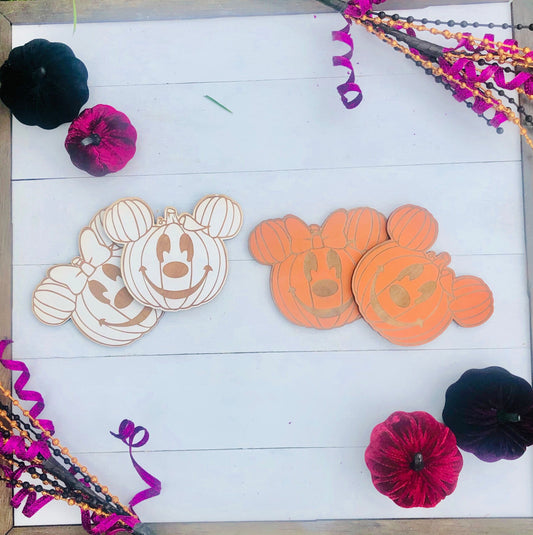 Two wooden pumpkin-shaped cutouts with Mickey Mouse design on a white wooden surface with Halloween decorations.