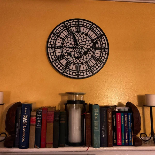 Decorative wall clock on a yellow wall above a shelf with books and a candle.